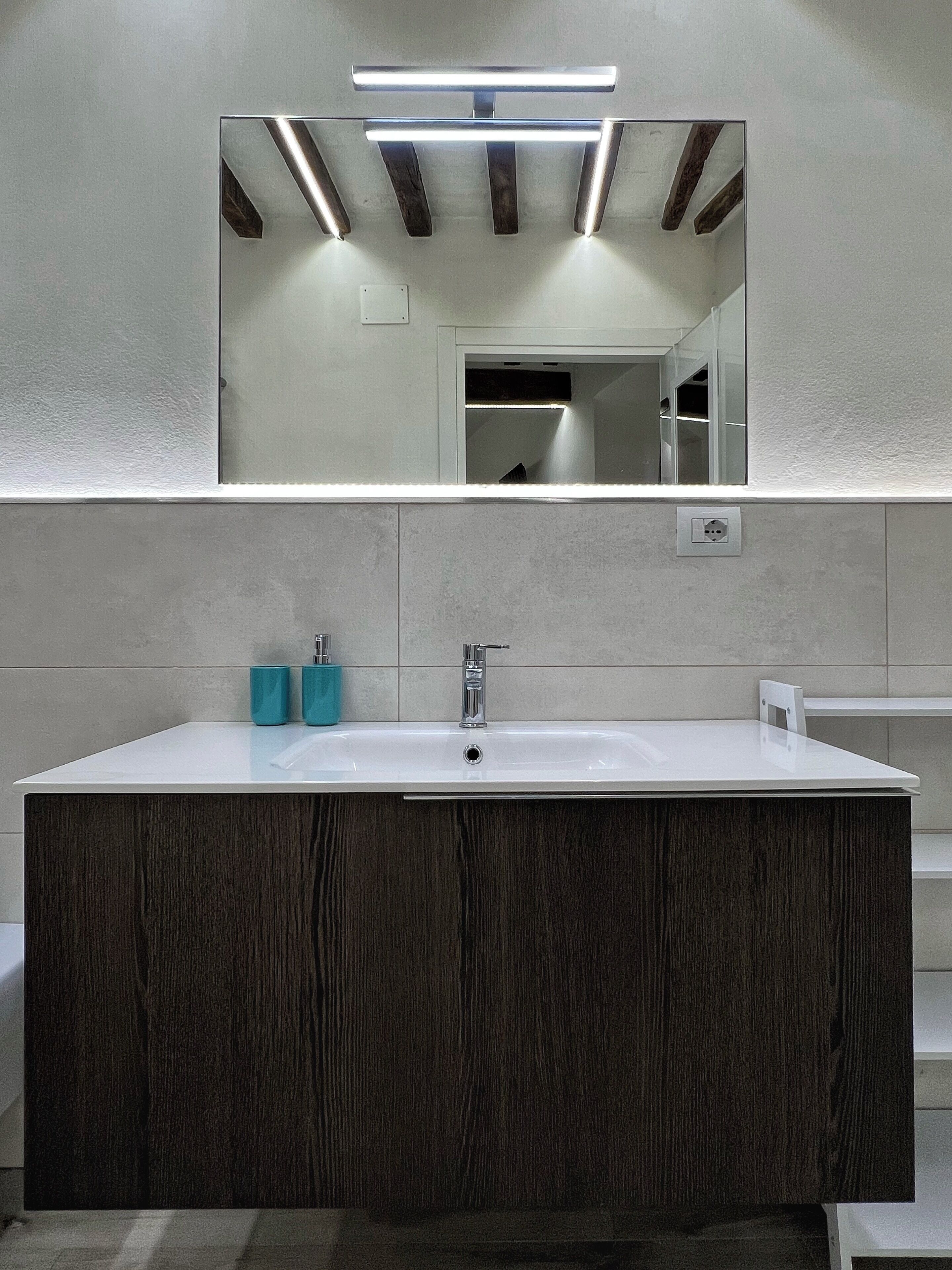 Een moderne badkamer met een grote rechthoekige wasbak, een donker houten wastafelmeubel en een spiegel met ingebouwde verlichting.