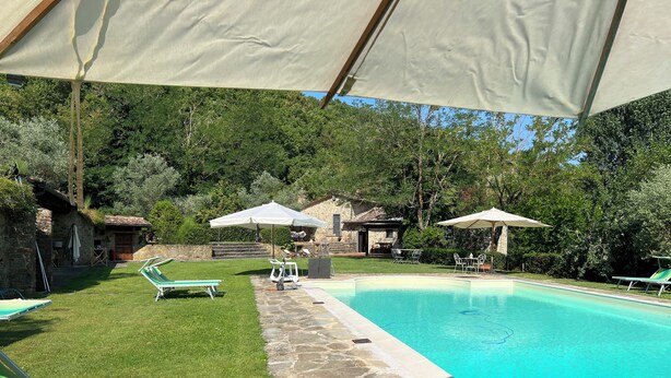 Une piscine entourée de murs de pierre et de verdure, avec des chaises longues et des parasols.