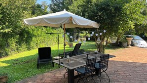 Une terrasse extérieure avec une table et des chaises, un parasol et des guirlandes lumineuses.