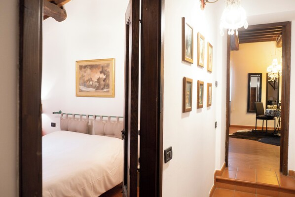 A hotel room with a bed, a painting on the wall, and a hallway leading to a dining area.