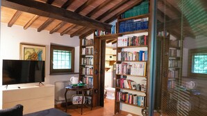 A cozy living room with a flat-screen TV, a sofa, a coffee table, and a bookshelf filled with books.