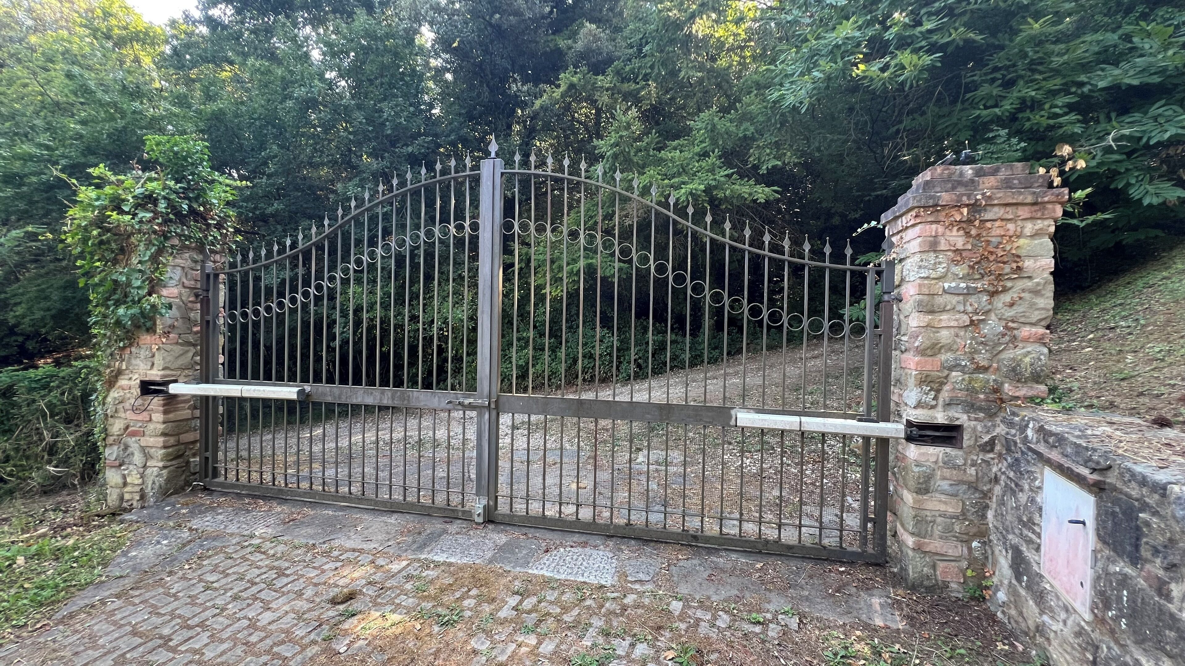 A gated entrance with a metal gate, stone pillars, and a brick wall.