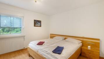 Une chambre à coucher avec un lit, une table de chevet, une fenêtre, un radiateur et un tableau au mur.