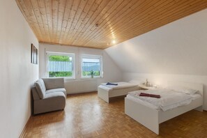 Camera da letto con soffitto in legno, due letti, un divano e due finestre con tende.