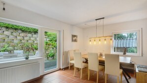 A dining area with a table and chairs, a radiator, and a view of greenery through a window. - Holiday Home Talblick / 160 m² / Up to 8 Guests / Garden / 2 Bathrooms / Sauerland (Schmallenberg)