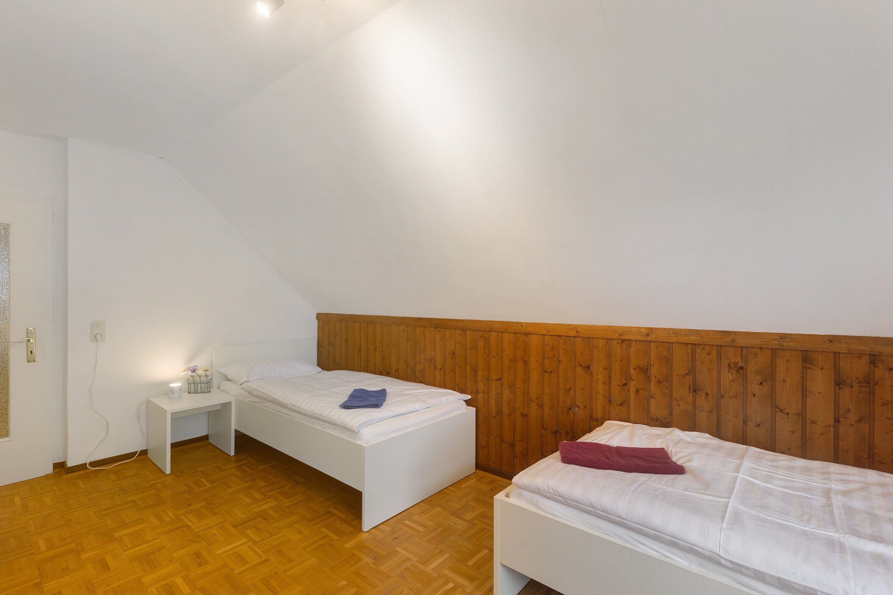 Une chambre avec deux lits, une tête de lit en bois, une table de chevet blanche et un plancher en bois.