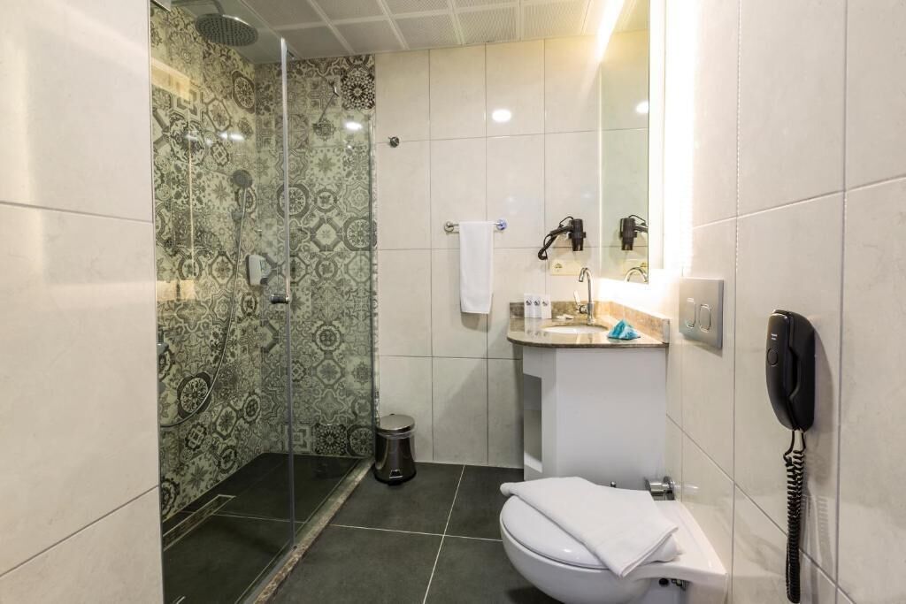 A bathroom with a shower, toilet, sink, and a telephone.