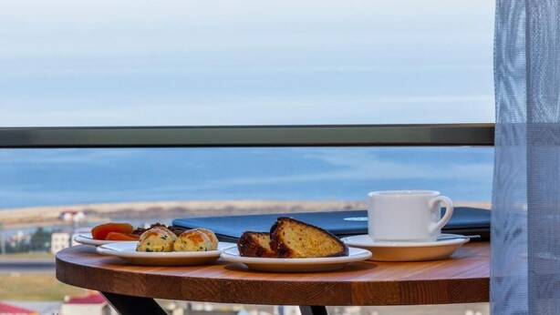 Una mesa con una taza y platillo blancos, un plato de pasteles y vista al mar.