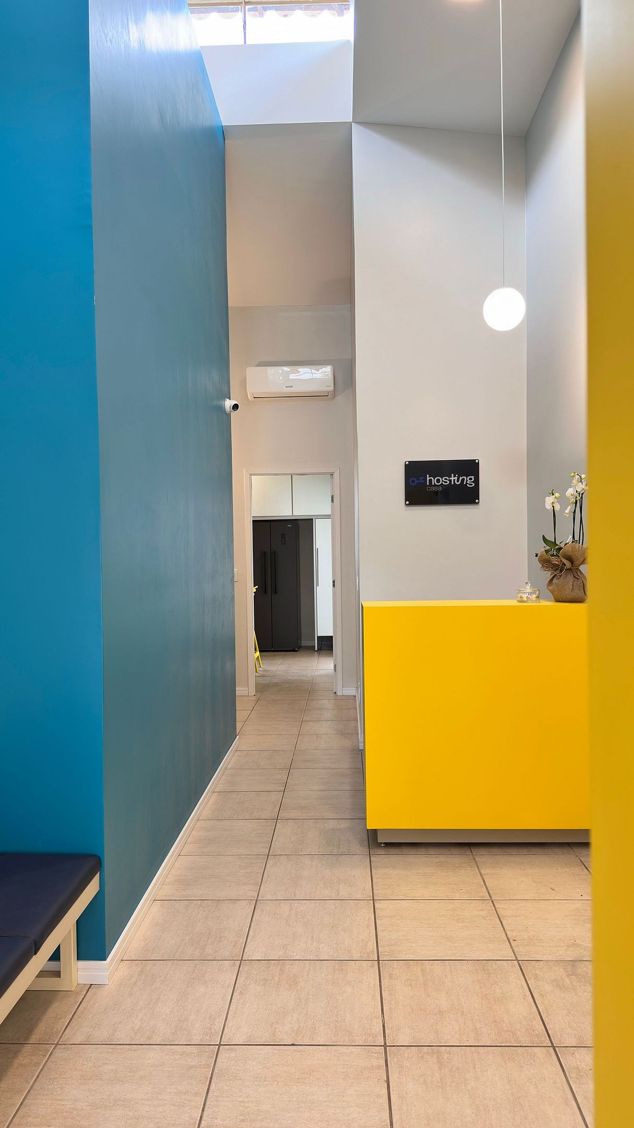 A hotel reception area with a blue wall, a yellow reception desk, and a sign that reads "hosting casa."