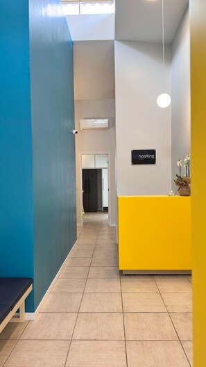 Zona de recepción de un hotel con una pared azul, un mostrador de recepción amarillo y un letrero que dice 'hosting casa'.