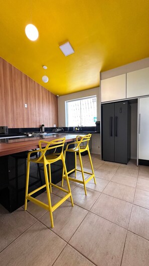 Una cocina con encimera de madera, un refrigerador negro y taburetes amarillos.