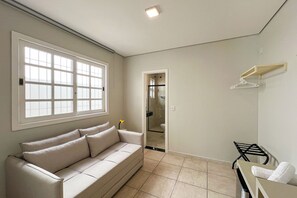 A room with a beige sofa, a window, a door leading to a bathroom, and a towel rack.