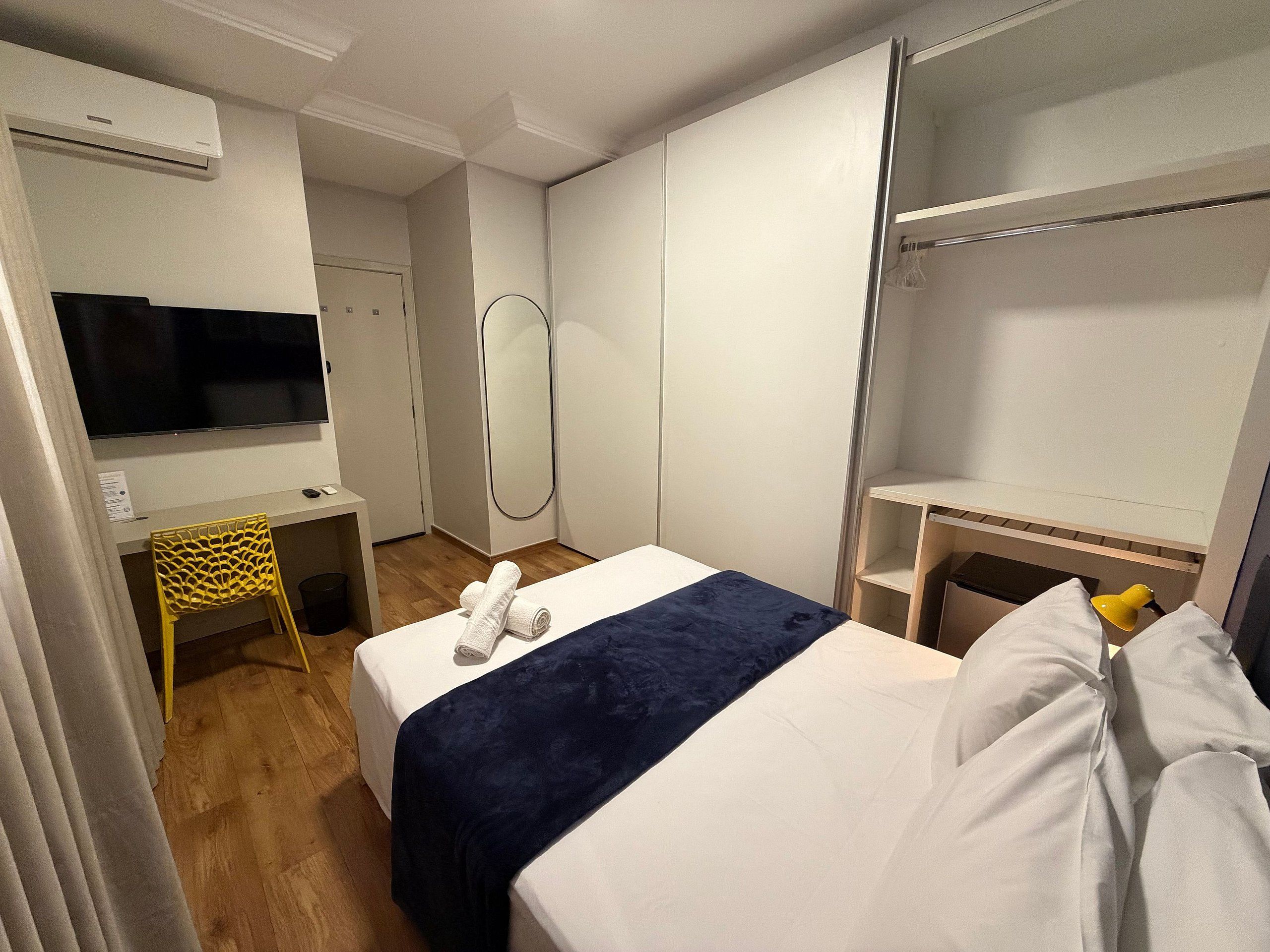 Une chambre d’hôtel équipée d’un lit, d’un bureau, d’une chaise, d’une télévision, d’un miroir et d’une armoire.