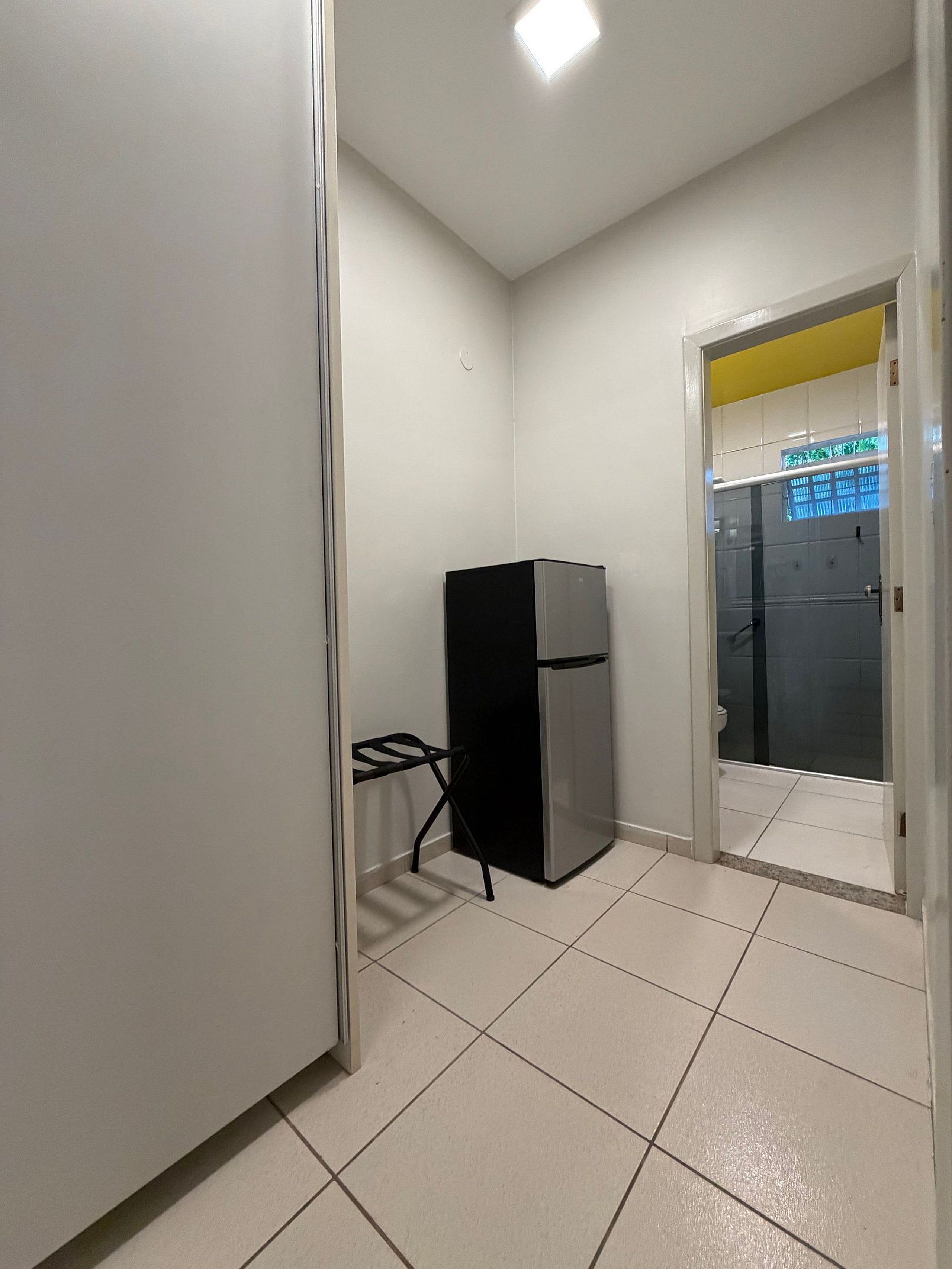 Une petite pièce comprenant un réfrigérateur, une petite table et une porte donnant sur une salle de bain.