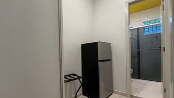Une petite pièce comprenant un réfrigérateur, une petite table et une porte donnant sur une salle de bain.