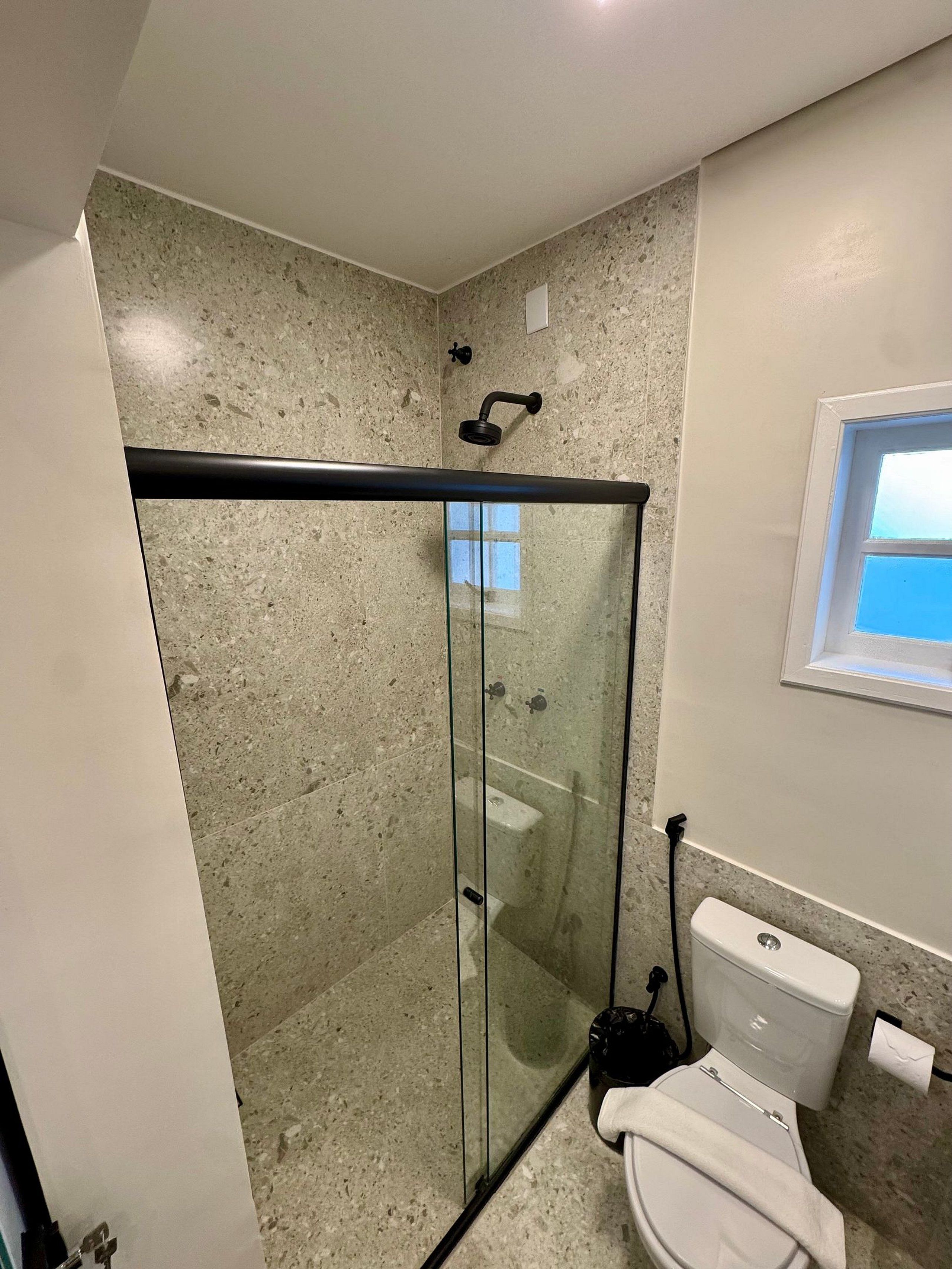 A modern bathroom with a glass-enclosed shower, a toilet, and a window.