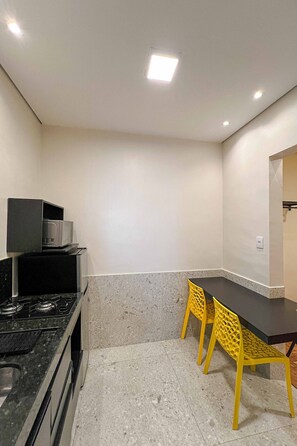A compact kitchen with a stove, microwave, and a dining area with yellow chairs.