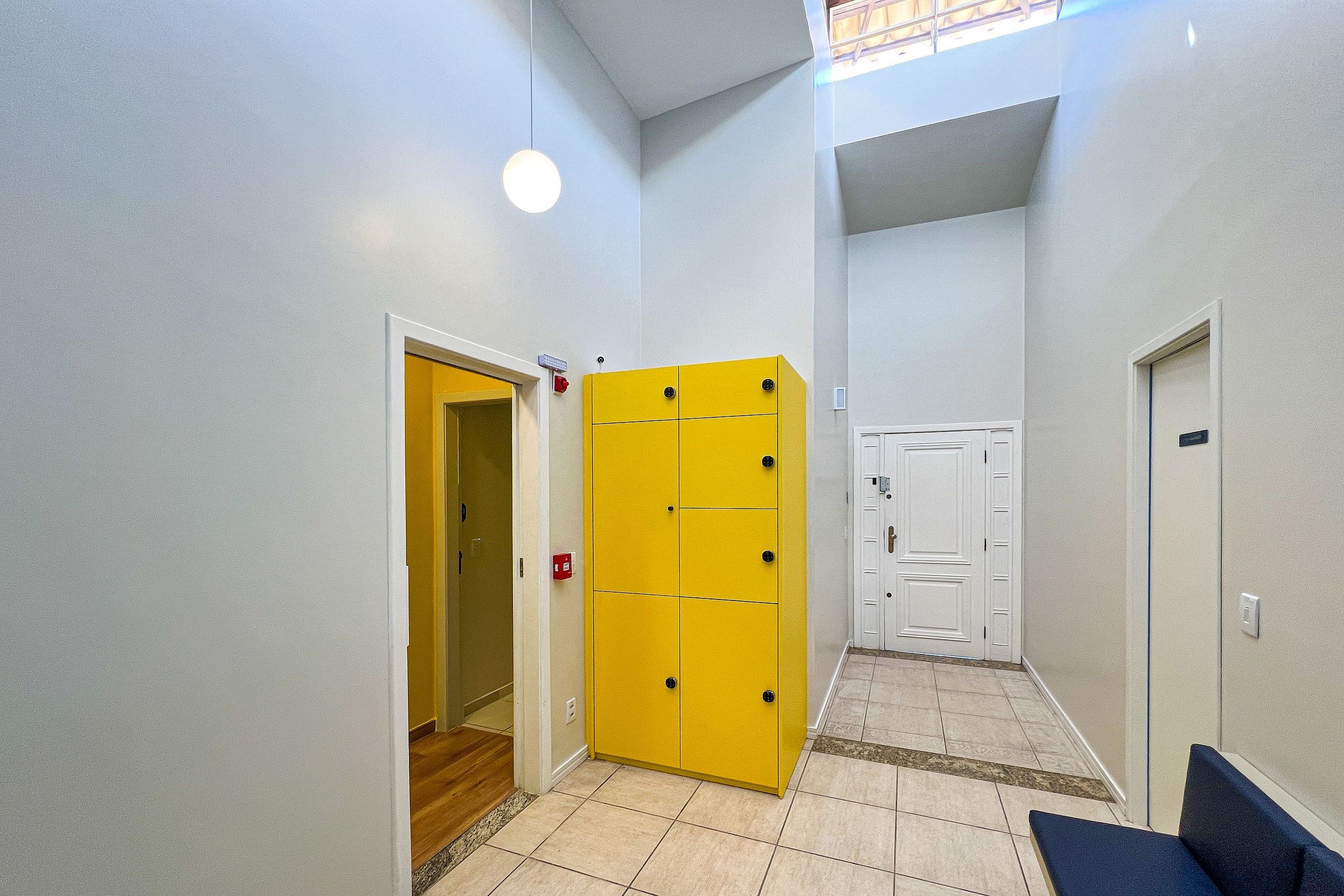 Un couloir avec un meuble de rangement jaune, une porte blanche et un banc bleu.