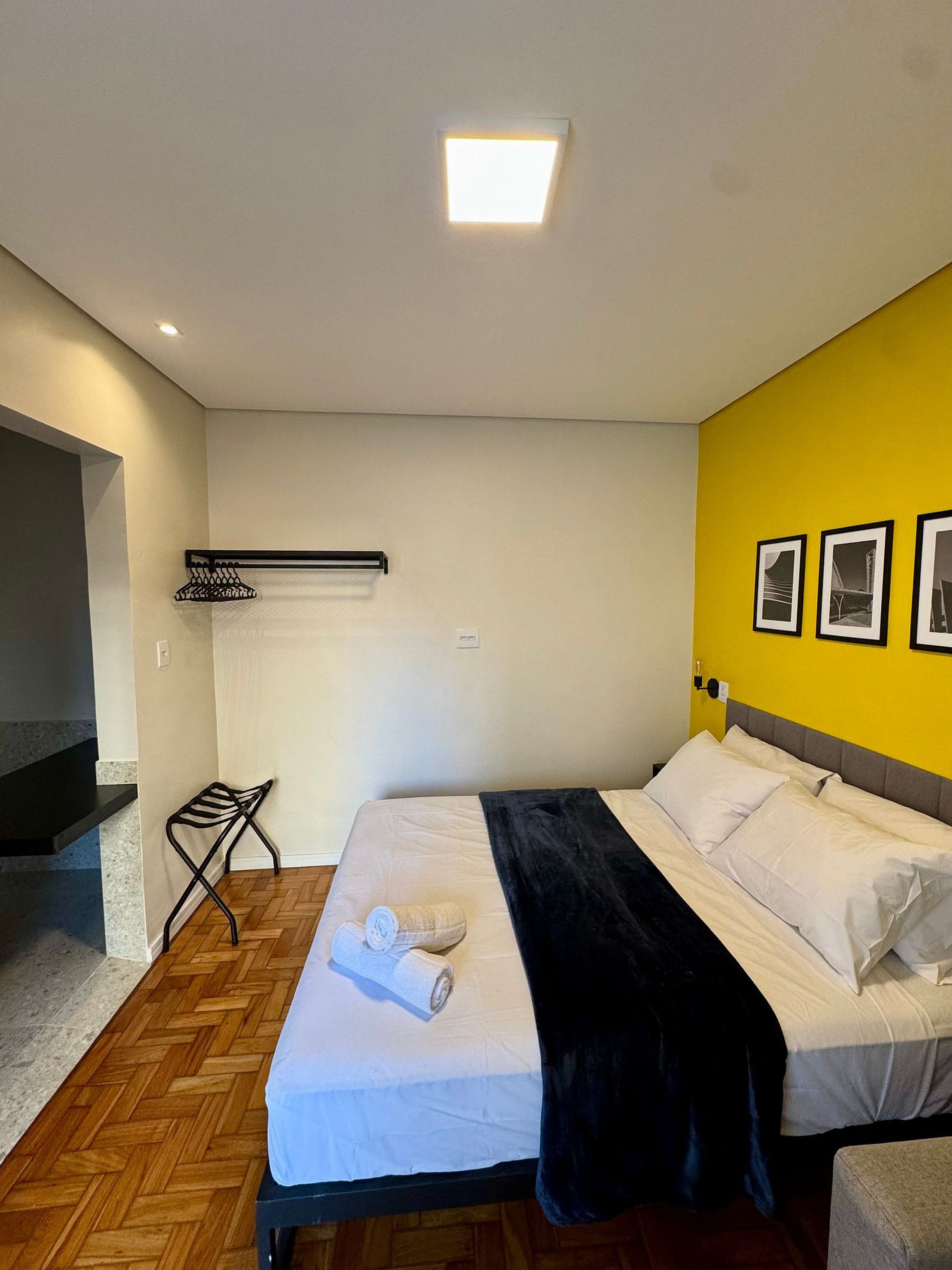 Una habitación de hotel con una cama, una silla negra, una toalla y una estantería.