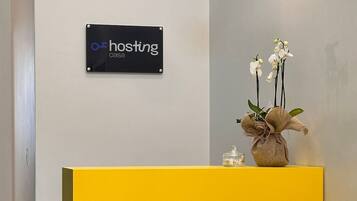 Ein Empfangsbereich mit einem gelben Schreibtisch, einem Schild mit der Aufschrift "hosting casa" und einer Vase mit weißen Blumen.