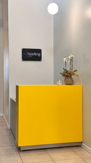 A reception area with a yellow desk, a sign that reads "hosting casa", and a vase with white flowers. - Casa Hosting (Belo Horizonte)