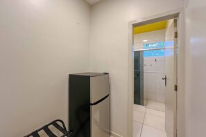 A room with a refrigerator, a door leading to a tiled area, and a bench.
