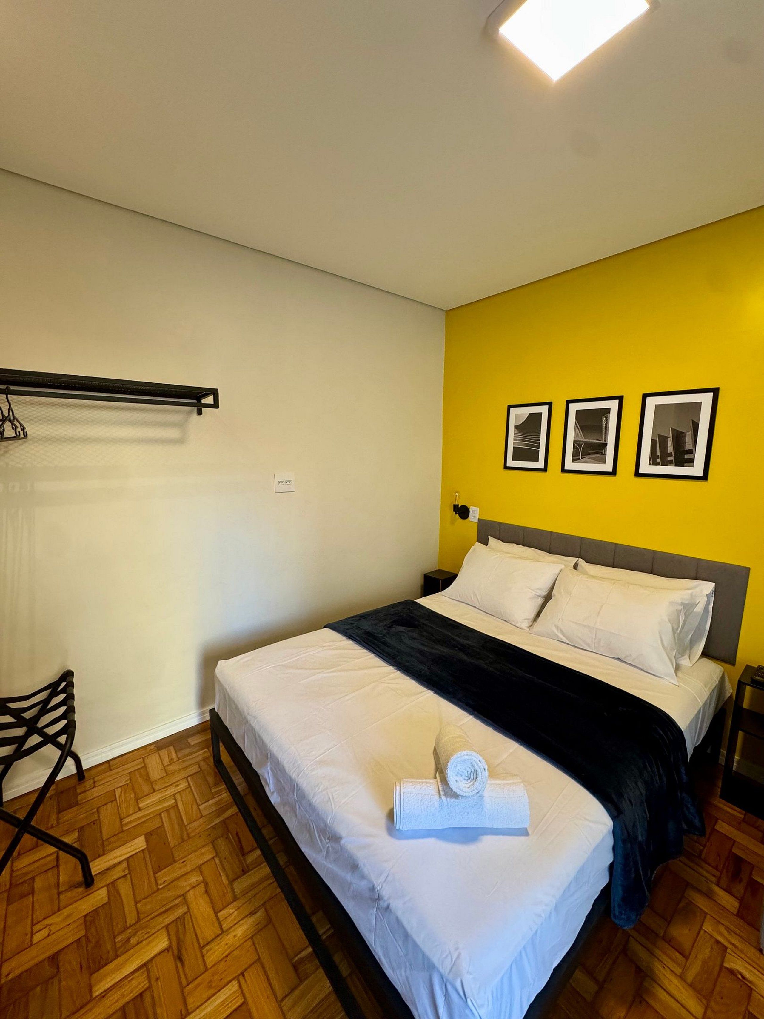 Habitación de hotel con cama, una silla, una mesita de noche y tres cuadros en la pared.