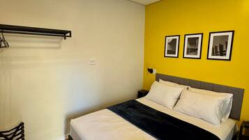 Habitación de hotel con cama, una silla, una mesita de noche y tres cuadros en la pared.
