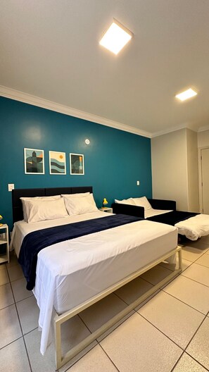 Quarto de hotel com duas camas, uma parede de destaque em tons de verde-água e obras de arte.