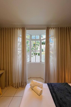 Ein Hotelzimmer mit großem Fenster, einem Bett mit einem zusammengerollten Handtuch und Vorhängen.