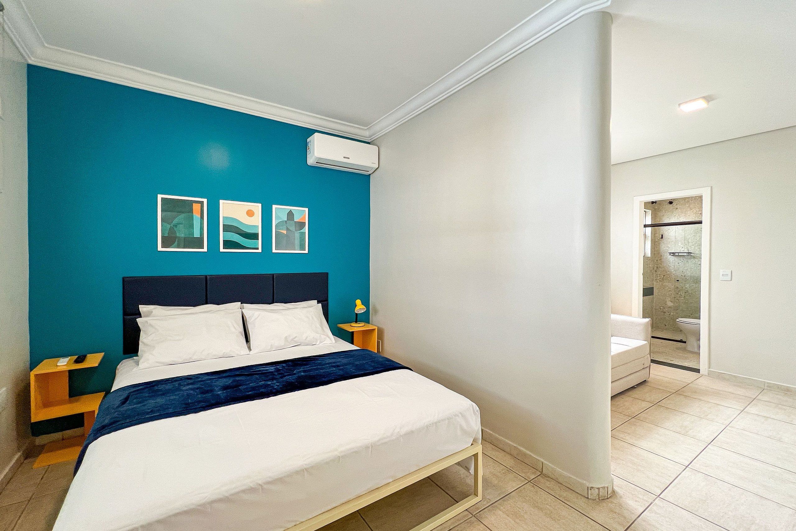 Un dormitorio con una cama, una mesita de noche, aire acondicionado de pared y obras de arte.