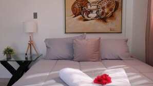 A neatly made bed with a rolled white towel and a red flower, a lamp on a side table, and a painting above the bed. - Live near the Colosseum! Apartment less than 20 min from the airport (San Juan)
