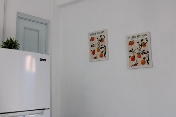 Une cuisine avec un réfrigérateur blanc et deux panneaux décoratifs fixés au mur, ornés de motifs de fruits d’agrumes.