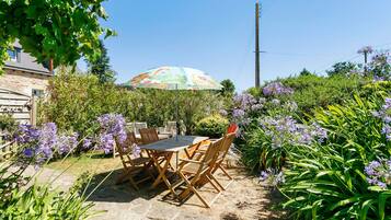 Eine Terrasse im Freien mit Tisch und Stühlen, umgeben von üppigem Grün und violetten Blumen.