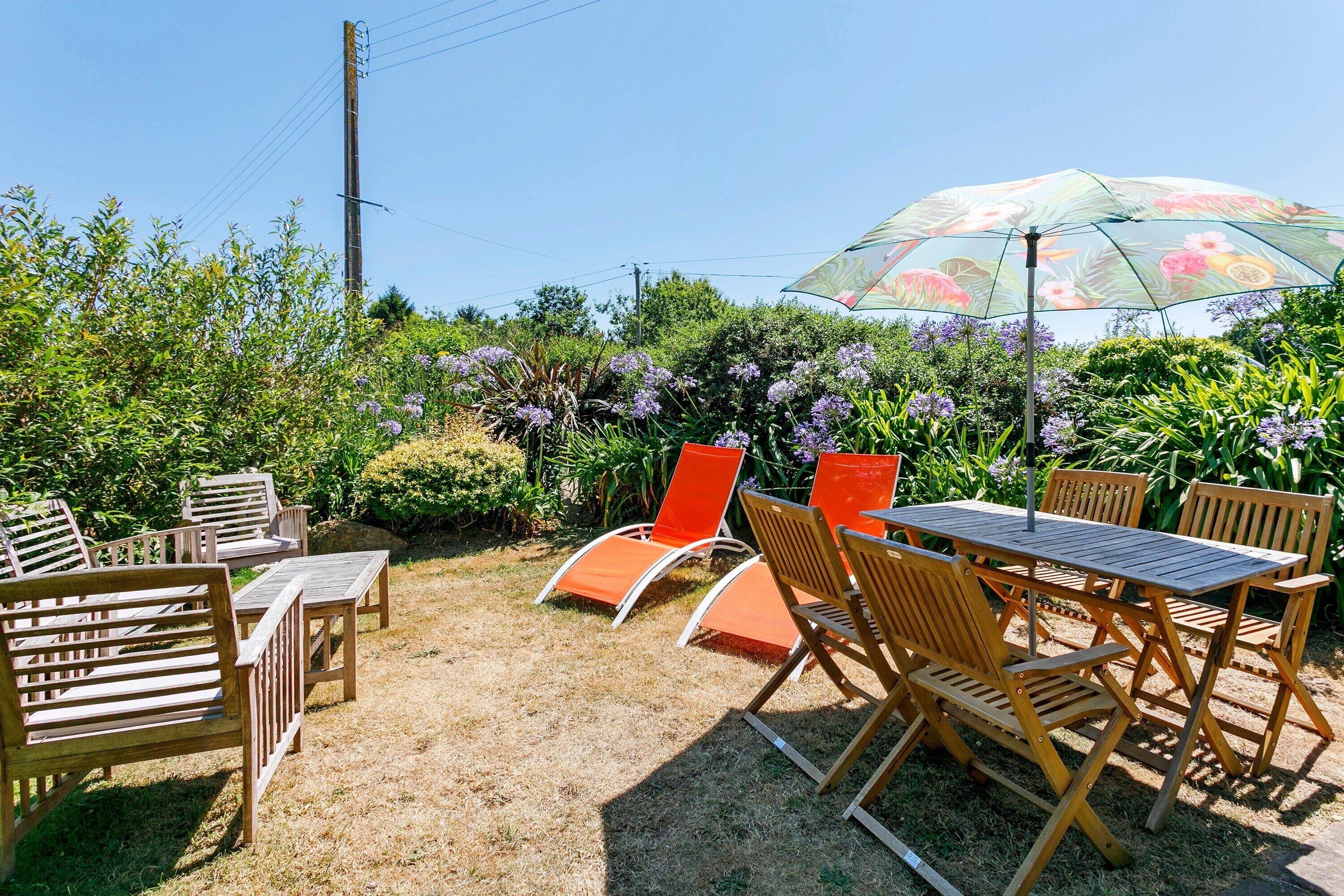 Un espace extérieur aménagé avec des meubles en bois et une table, entouré d’une végétation luxuriante et de plantes en fleurs.