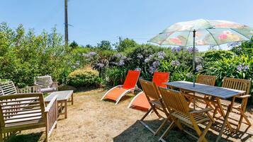 Un espace extérieur aménagé avec des meubles en bois et une table, entouré d’une végétation luxuriante et de plantes en fleurs.