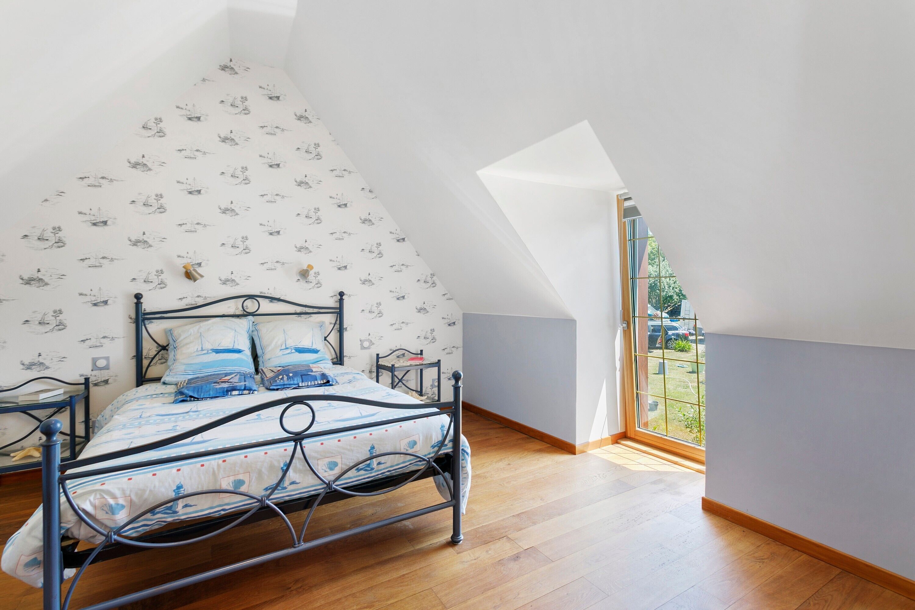 Una camera da letto con soffitto spiovente, un letto con struttura in metallo e una finestra vista aperta.