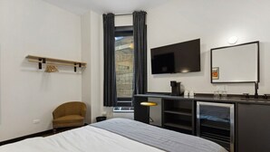A hotel room with a bed, a desk with a chair, a TV, and a window with curtains. - Logan Square SRO Hotel (Chicago)