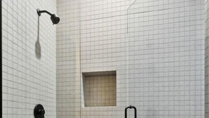 A glass-enclosed shower area with a tiled floor and walls, a handheld showerhead, a wall-mounted control, and a towel ring. - Logan Square SRO Hotel (Chicago)