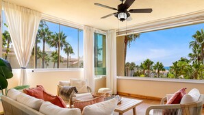 A balcony with wicker furniture, a ceiling fan, and a view of palm trees.