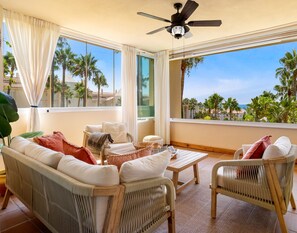 A balcony with wicker furniture, a ceiling fan, and a view of palm trees.