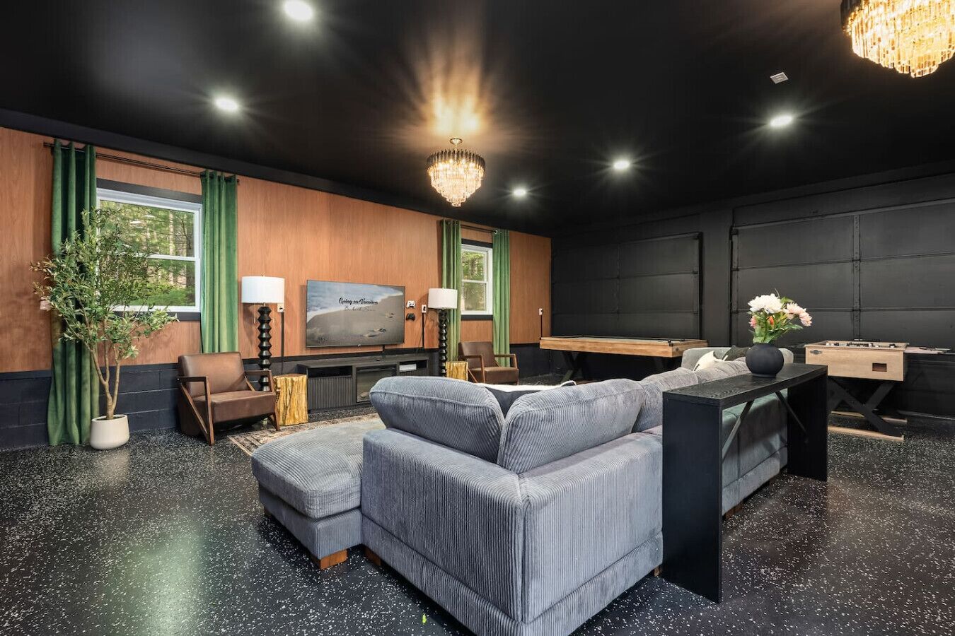 A modern living room with a grey sectional sofa, a flat-screen TV, a chandelier, and a foosball table.
