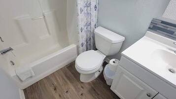 Een badkamer met een wit toilet, een badkuip en een wastafel met een spiegel erboven.