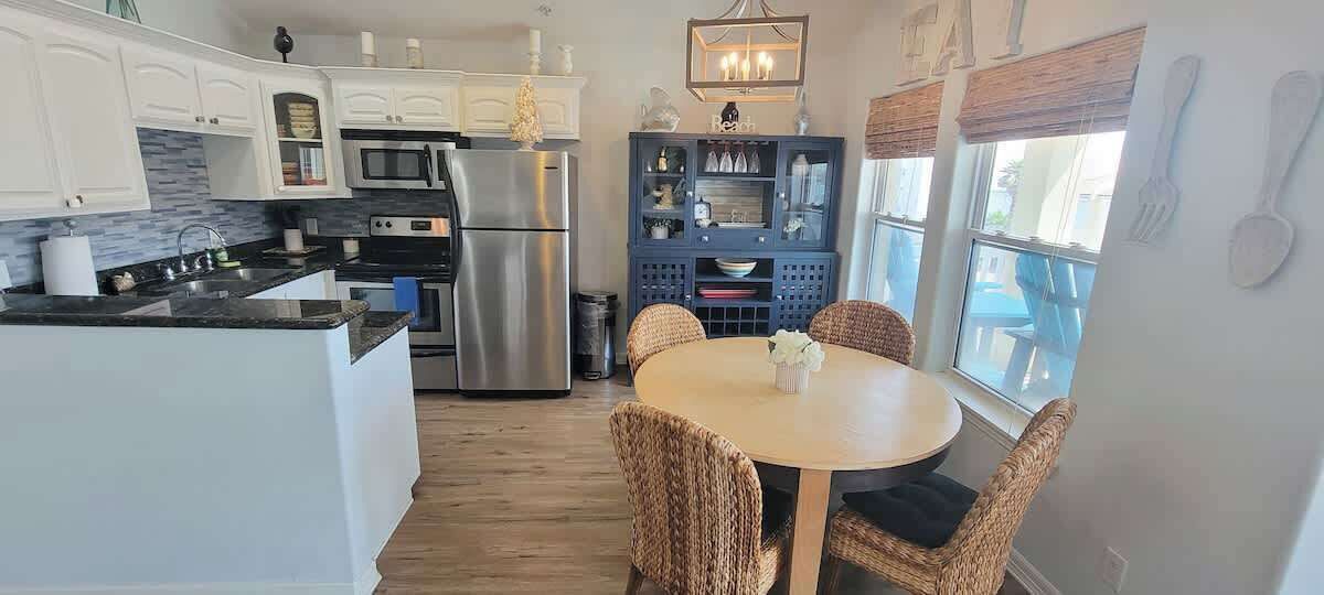 A modern kitchen with white cabinets, stainless steel appliances, and a dining area with wicker chairs.
