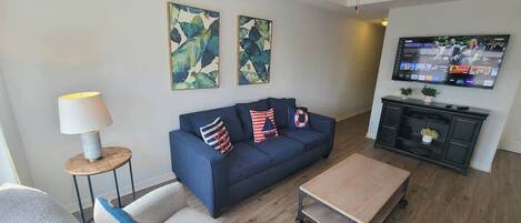 A living room with a blue sofa, a coffee table, a TV, and artwork on the wall.