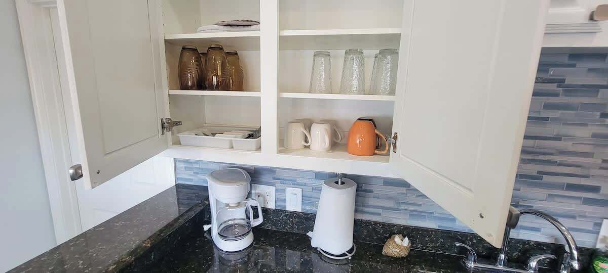 A kitchen with open cabinets displaying kitchenware, a coffee maker, and a kettle.