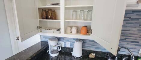 A kitchen with open cabinets displaying kitchenware, a coffee maker, and a kettle.