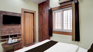 Ein Hotelzimmer mit Bett, Wandfernseher, Holzschrank und einem Fenster mit Vorhängen.