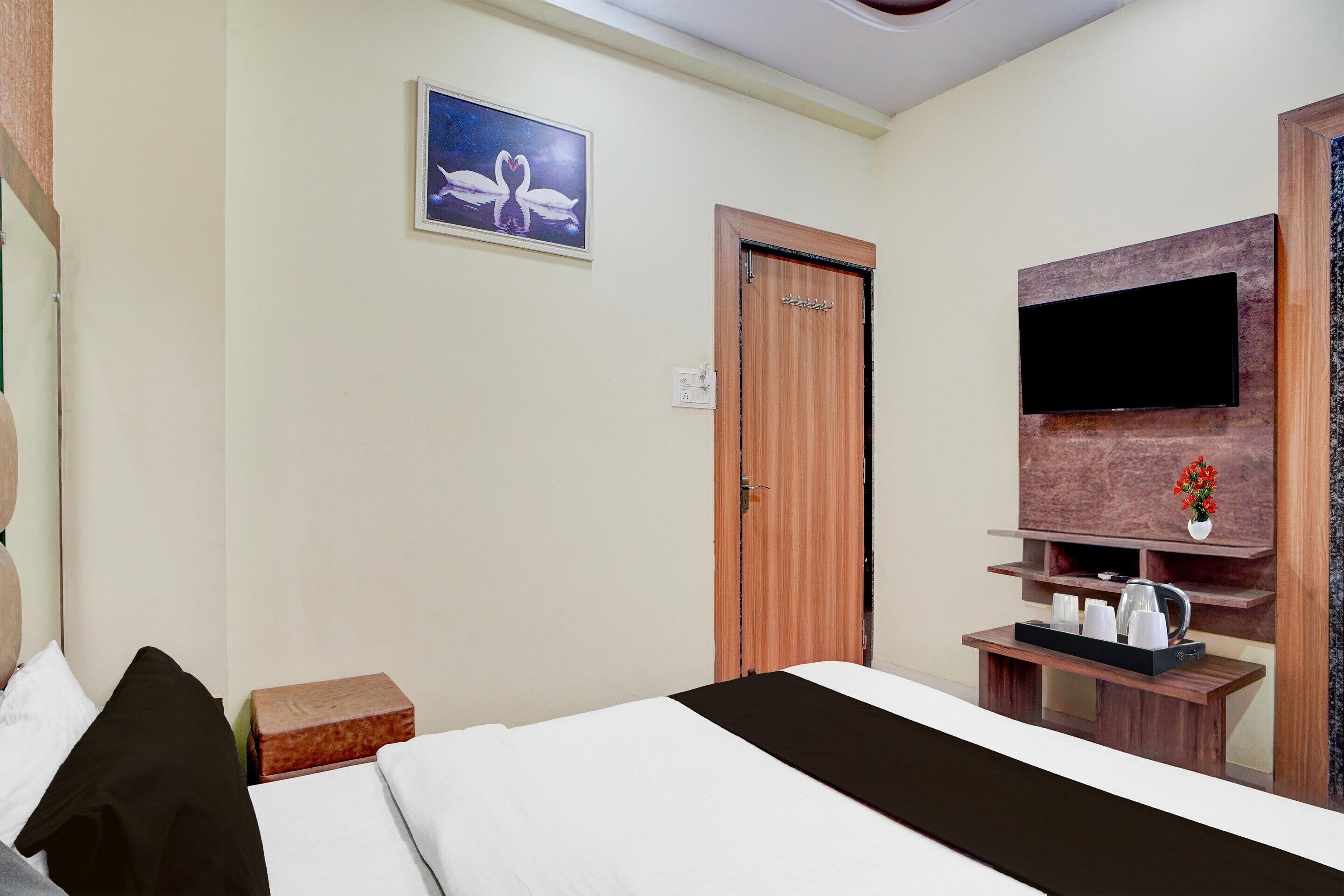 Habitación de hotel con cama, puerta de madera, televisor montado en un panel de madera y una mesita con bandeja.