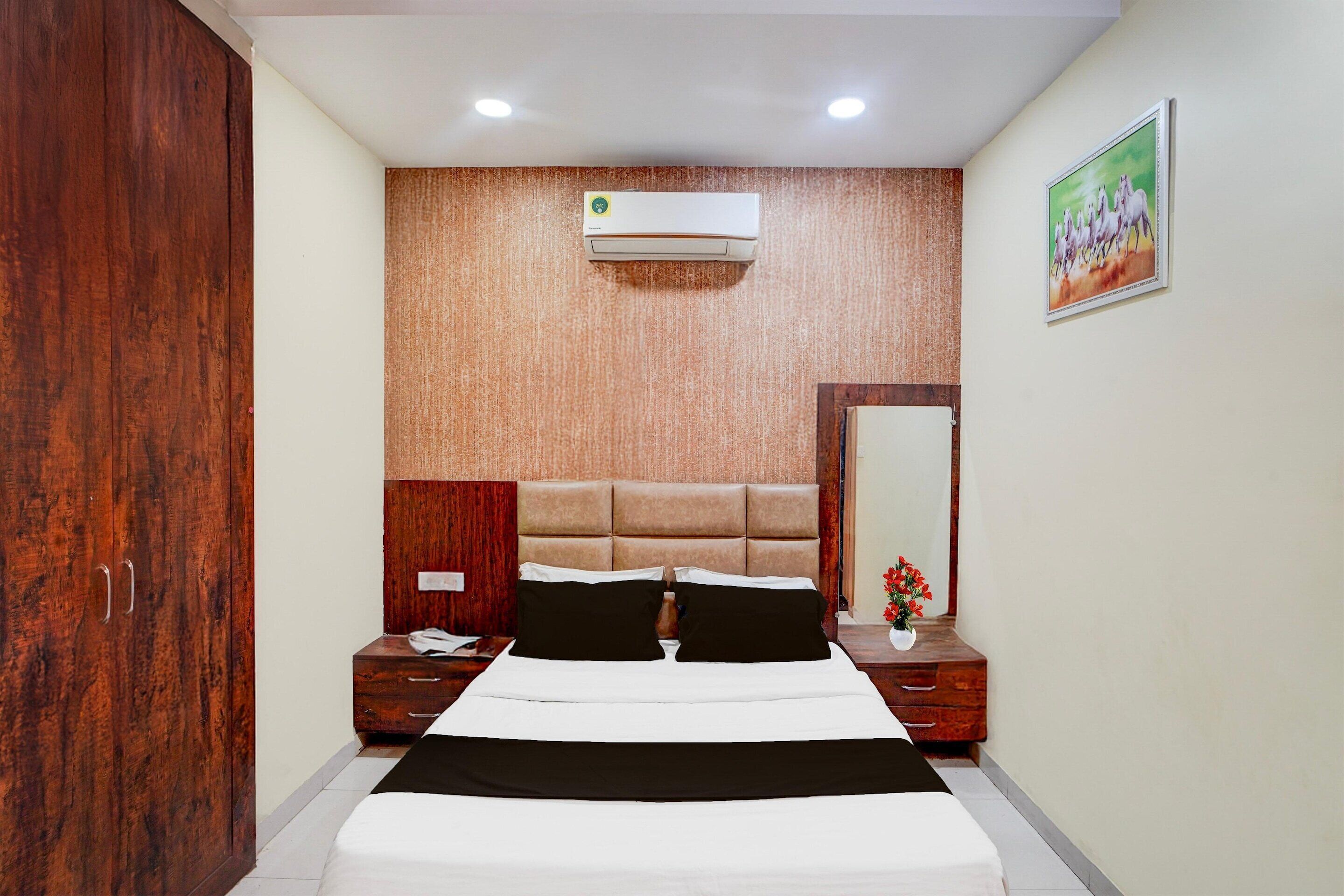 A bedroom with a bed, wooden wardrobe, bedside tables, an air conditioner, and a painting on the wall.